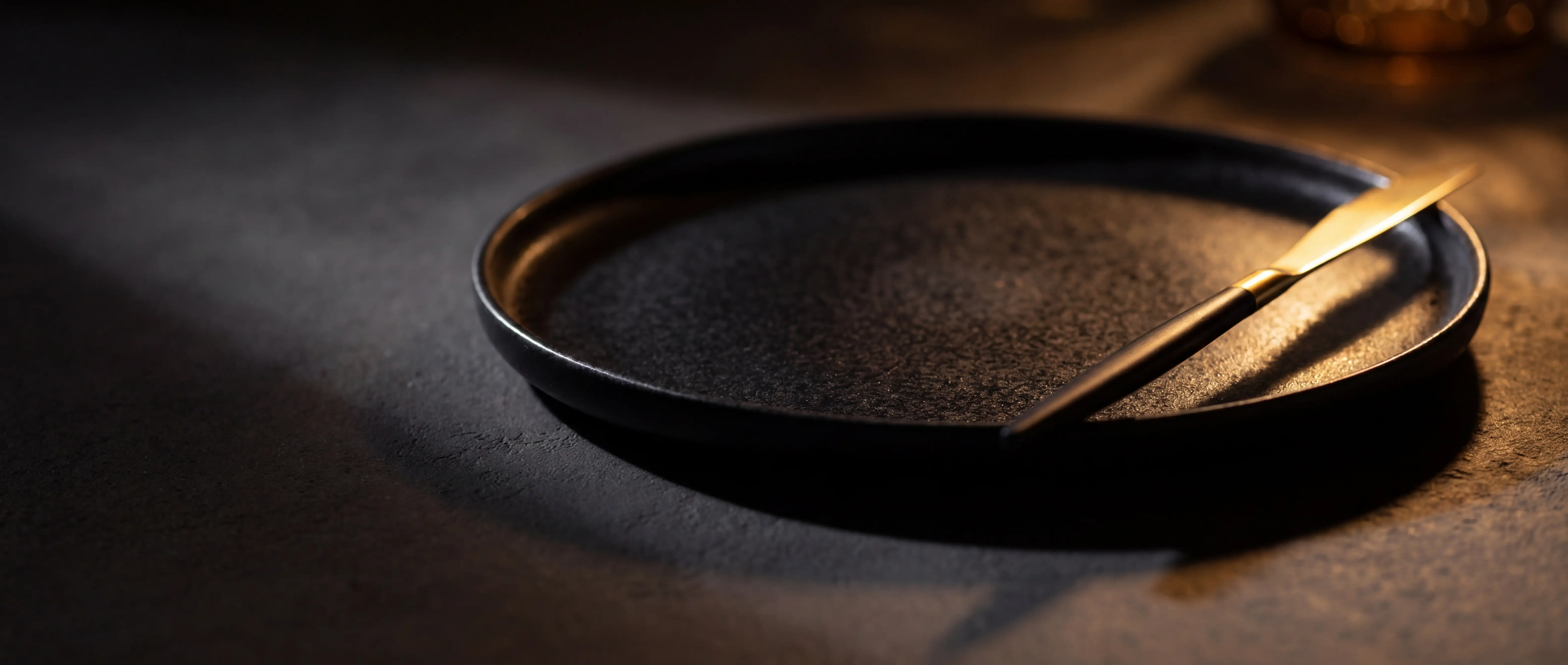 Premium matte black melamine plate with gold knife on dark surface, dramatic lighting